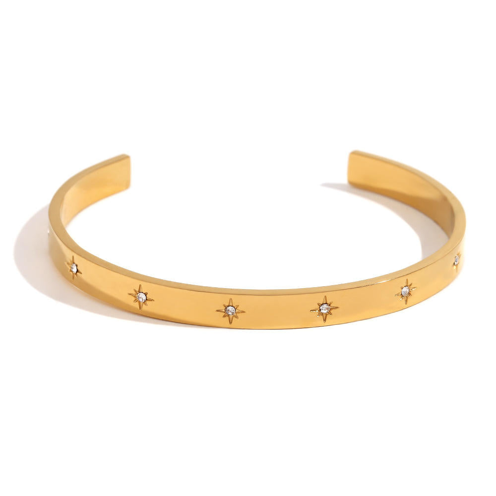 A gold open cuff bracelet featuring five small starburst motifs set with clear stones, photographed on a clean white background.
