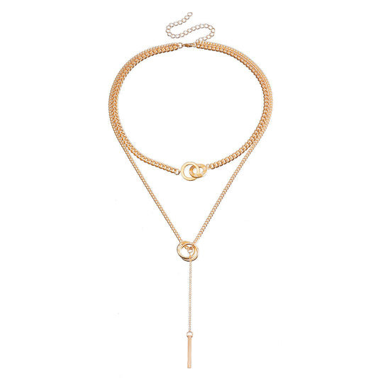 A gold-toned multi-layer necklace featuring a thick curb chain, a delicate chain with a small interlocking ring, and a long lariat drop ending in a flat bar, displayed on a solid white background.